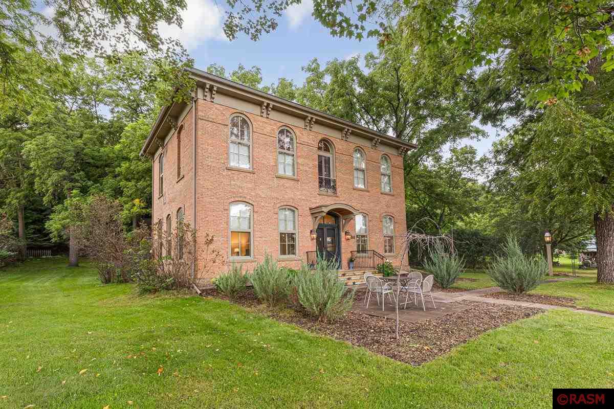 This 1875 Italianate, solid brick, 4 bds, 4-1/2 baths home is an architectural gem. You approach under a copper-clad portico, up Kasota stone steps with custom wrought iron rails. Entering through the original French doors, you are impressed by 11-ft ceilings. The LR invites you with light from 7-1/2 ft windows. The gas fireplace makes a cozy spot for relaxing. The DR is a pleasant space for dinners. Entering the kitchen, you’ll find open cabinets, 2 porcelain sinks, and butcher block counters. An open staircase leads you to the 2nd level with 3 beds and 2 baths. The 3rd level holds an ensuite quarters, with light from 4 skylights. The 0.9 acre lot is set on a wooded hillside above Henderson, providing grand views of the Minnesota River Valley. Twelve mature black walnut trees provide ample shade. The backyard houses an 1850s log cabin with elec and heat. A fire pit area and country garden adjoin the cabin. An attached screen porch and Kasota stone patio are at the back of the home.